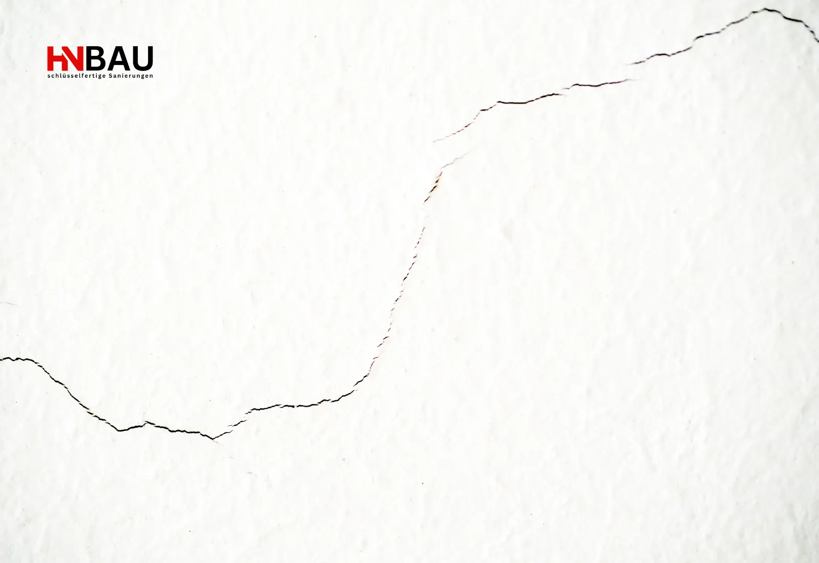 Feiner Riss in einer weißen Innenwand, der eine typische Schadstelle zeigt, die durch Spachtelarbeiten ausgebessert werden muss.